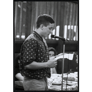A young man stands at a microphone, reading from a piece of paper at a Kiwanis Awards Night