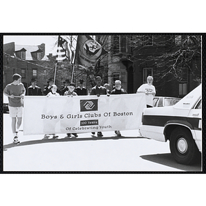 Four boys and two girls marching with a large banner with the text "Boys and Girls Clubs of Boston 100 Years Of Celebrating Youth," followed by the USS Constitution Color Guard team during the parade