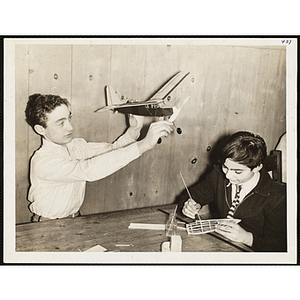 A boy holds up a model aircraft while another builds a new model for his arts and crafts class at the Boys' Clubs of Boston