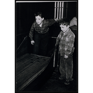 A boy plays a bowling game as another boy looks on