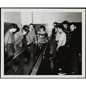 A boy plays a table game as a man and other boys look on in the South Boston Clubhouse