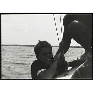 A man pulls a boy up from the side of a sailboat in Boston Harbor