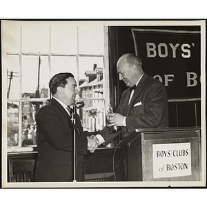 Arthur T. Burger, Executive Director of Boys' Clubs of Boston, holds a trophy and shakes hands with State Senator John E. Powers at a Boys' Clubs of Boston awards event