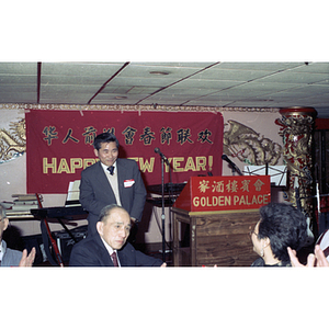 Man stands next to a podium in front of a large group gathering for a celebration of the Chinese New Year