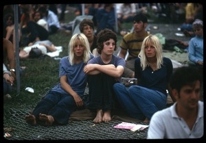 Three women seated on a fallen chain link fence at the Woodstock Festival
