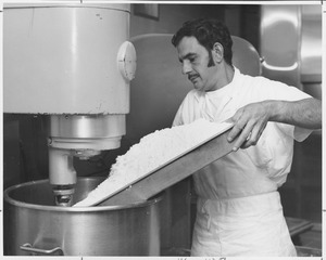 Robert Sacco adding flour to large bread mixer