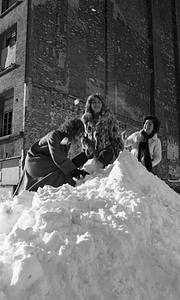 Three women throwing snowballs atop large snowpile