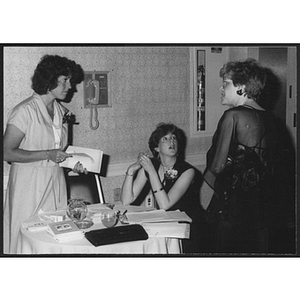 Women in formal dress standing and sitting around table at auction event