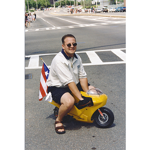 A man rides a tiny motorcycle during a parade