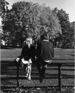 A female and male student sit on the Science Quad fence, 1969