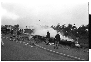 Firefighters putting out fire in travellers' caravan and portacabin on Flying Horse Road, Downpatrick, while traveller children "clown" at the camera.  Members of the "settled" community were blamed for the arson