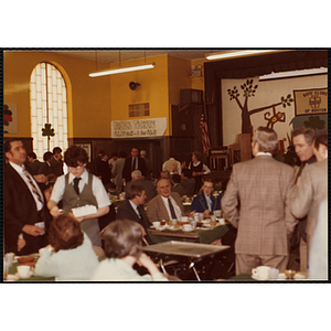 Several guests buying raffle tickets in the distance while others sit and stand around tables during a Boys' Club St. Patrick's Day event