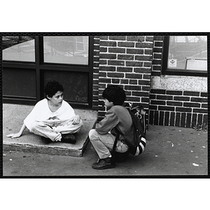 Two boys sit outside and talk in front of the Charlestown Boys and Girls Club building