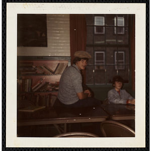 A young man wearing a hat sits on a table and looks at the camera at the South Boston Boys' Club