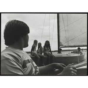 A teenage boy in a boat sails past five teenagers on another sailboat in Boston Harbor