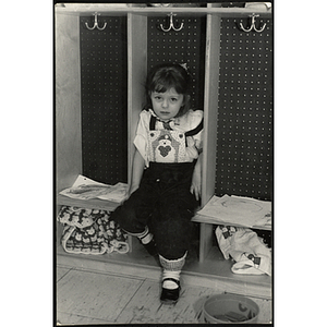 A girl sits on a shelf in a cubby