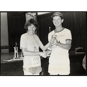 A woman and man shakes hands and pose with a trophy during the Battle of Bunker Hill Road Race