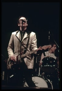 Elvis Costello and the Attractions in concert: Costello on guitar and vocals (drummer Bruce Thomas in background)