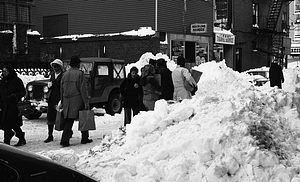 Pedestrians carrying bags among snow piles on Parameter Street