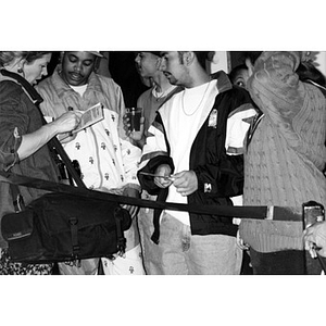Young people gathered around a female reporter with a large camera bag slung over her shoulder.