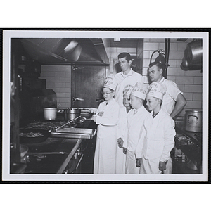 Four members of the Tom Pappas Chefs' Club participate in cooking at a stove as two Brandeis University kitchen staff members look on