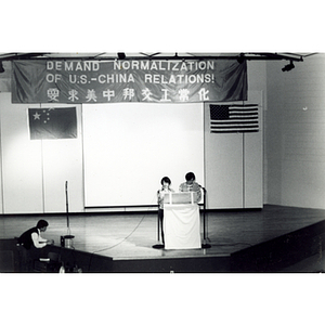 Two people talk onstage at the Josiah Quincy School at an event demanding the normalization of diplomatic relations between the United States and China