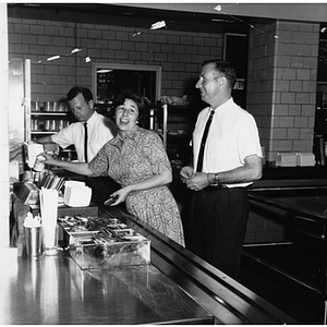 A woman and two men stand in an Ell Student Center cafeteria (?)