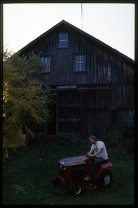 Peter Natti riding a lawnmower in front of the barn, Montague Farm Commune