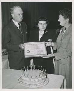Bruce Barton presents a woman with a certificate in front of a woman on crutches at the Institute for the Crippled and Disabled's 35th anniversary Red Cross luncheon