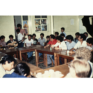 Group sitting around tables listening to men playing guitar