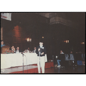 Jason Gallagher holds a microphone and looks down at his notes while the guests look on during the "Recognition Dinner at Harvard Club"