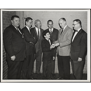 A boy receives a trophy while surrounded by the Boys' Club board members