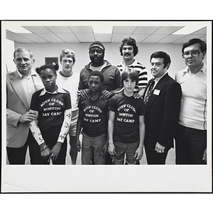 Six men, including John M. Durkin, at far left, posing with a girl and two boys wearing Boys' Clubs of Boston Day Camp t-shirts at a Boys' Club's event with New England Patriots