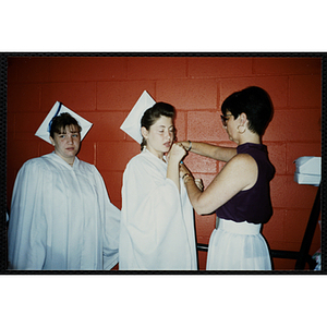 A woman affixes a boutineer to an Edwards School graduate's gown