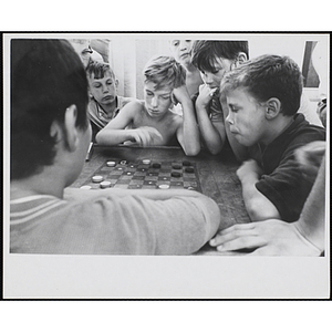 Two boys play checkers as other boys look on