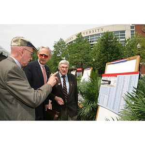 Three men look at the plans for the Veterans Memorial as they converse at the groundbreaking ceremony