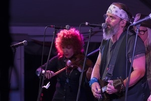 Steve Earle (guitar), Chris Masterson (guitar, obscured), and Eleanor Whitmore (fiddle) performing onstage with Steve Earle and the Dukes at the Payomet Performing Arts Center