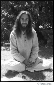 Gangadhar: portrait of the tabla player with Amazing Grace and member of Ram Dass satsang, smiling and seated in a lotus position in front of a rhododendron