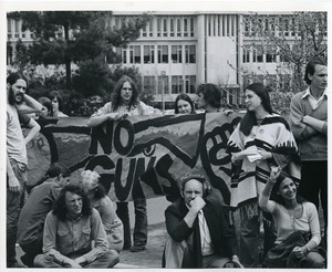 Board of Trustees fee increase demonstration: portestors gathered around a banner that reads, 'no guns'