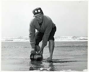 Unidentified man on a beach scooping with a tin can