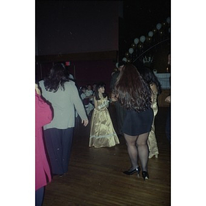 A girl in a gold dress and long gloves stands in the hall at the Jorge Hernandez Cultural Center, surrounded by people.