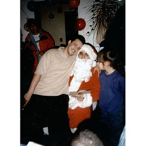 Young man sitting with a person dressed up as Santa Claus.