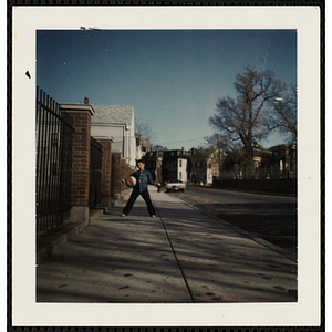 A boy posing with a basketball under his arm on the street outside the South Boston Boys' Club
