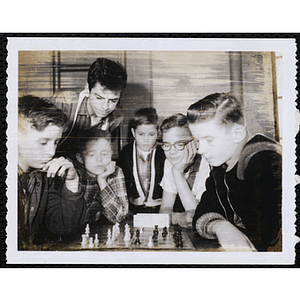Two boys play chess as four other boys look on