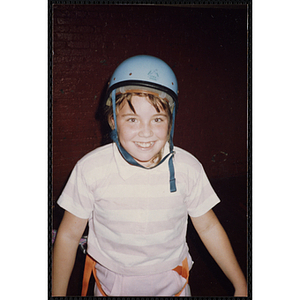 A girl in a gymnasium wears a safety harness and helmet