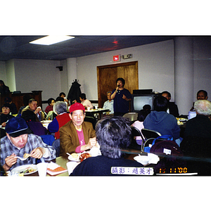 Guests sit at tables at a Thanksgiving dinner held at Association headquarters, with some laughing as they listen to a woman speak into a microphone