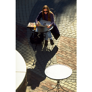 Student reading newspaper at table in the Snell Library courtyard