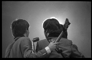 Rear view of (l. to r.) Paul McCartney, John Lennon, and George Harrison (obscured) huddled around a microphone in concert with the Beatles, Washington Coliseum