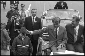 Robert F. Kennedy (left) seated in an open car at the Turkey Day parade, patting a boy on the head; while stumping for Democratic candidates in the northern Midwest