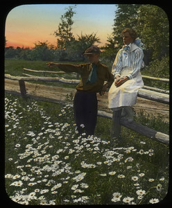Boy and girl on a wooden fence overlooking a field of ox eye daisies
